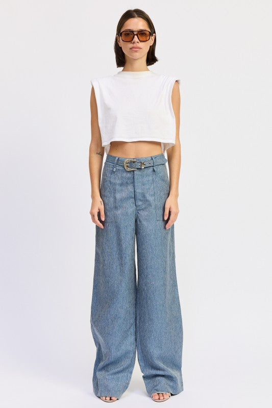 Woman wearing a white sleeveless top and blue wide-leg jeans on a white background