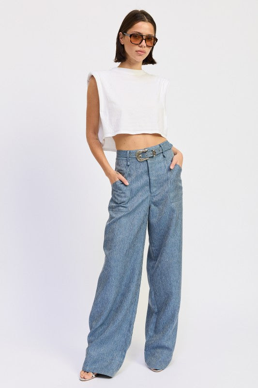 Woman wearing a white sleeveless top and blue high-waisted jeans on a white background