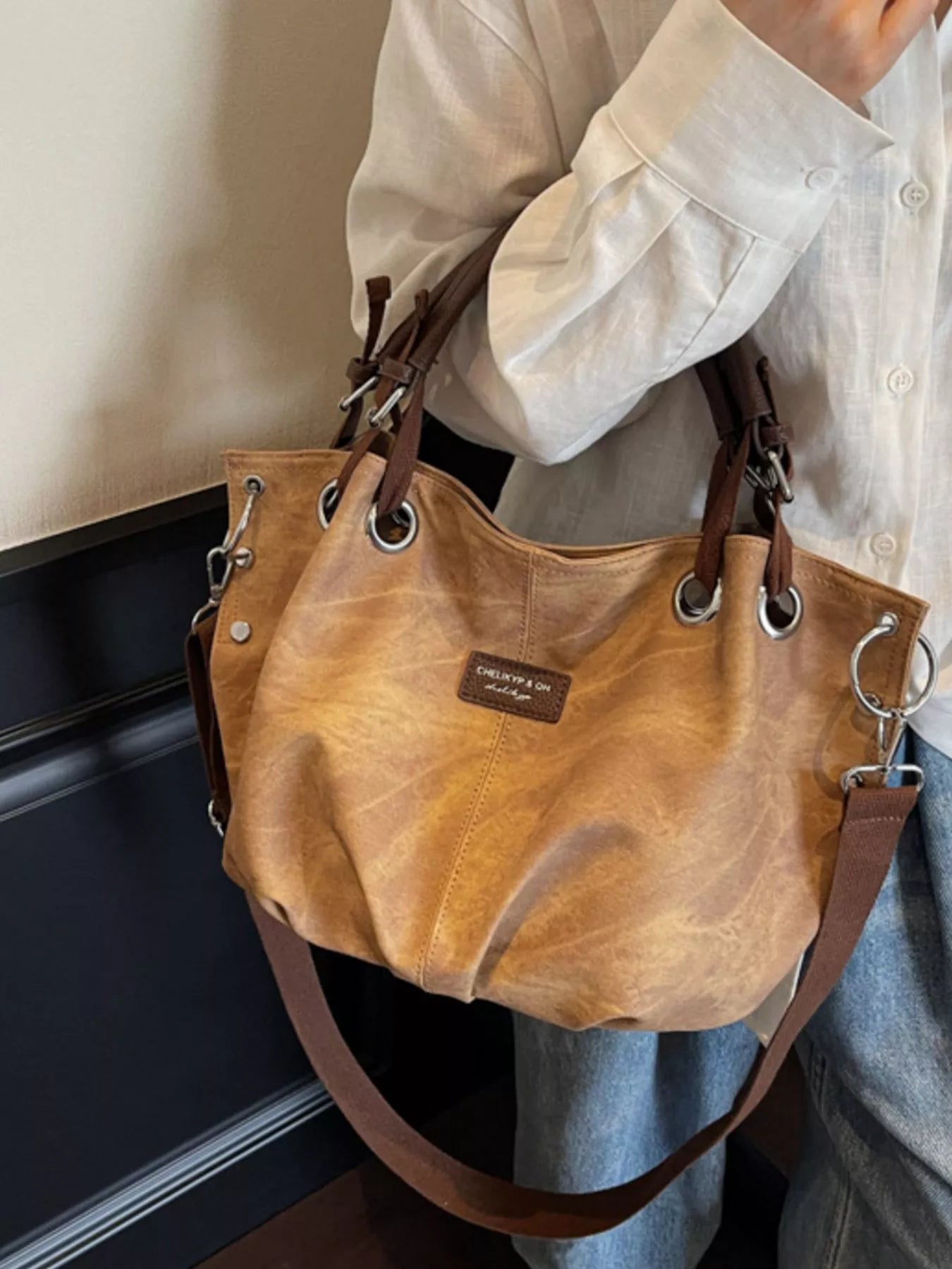 Brown leather handbag held by a person wearing a light-colored shirt and jeans.
