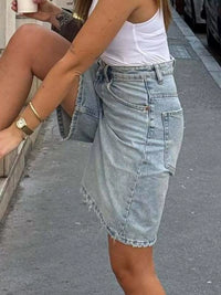 Person wearing a white tank top and denim shorts on a street.