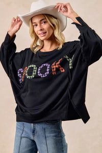 Woman wearing a black sweatshirt with colorful text, holding a white hat.