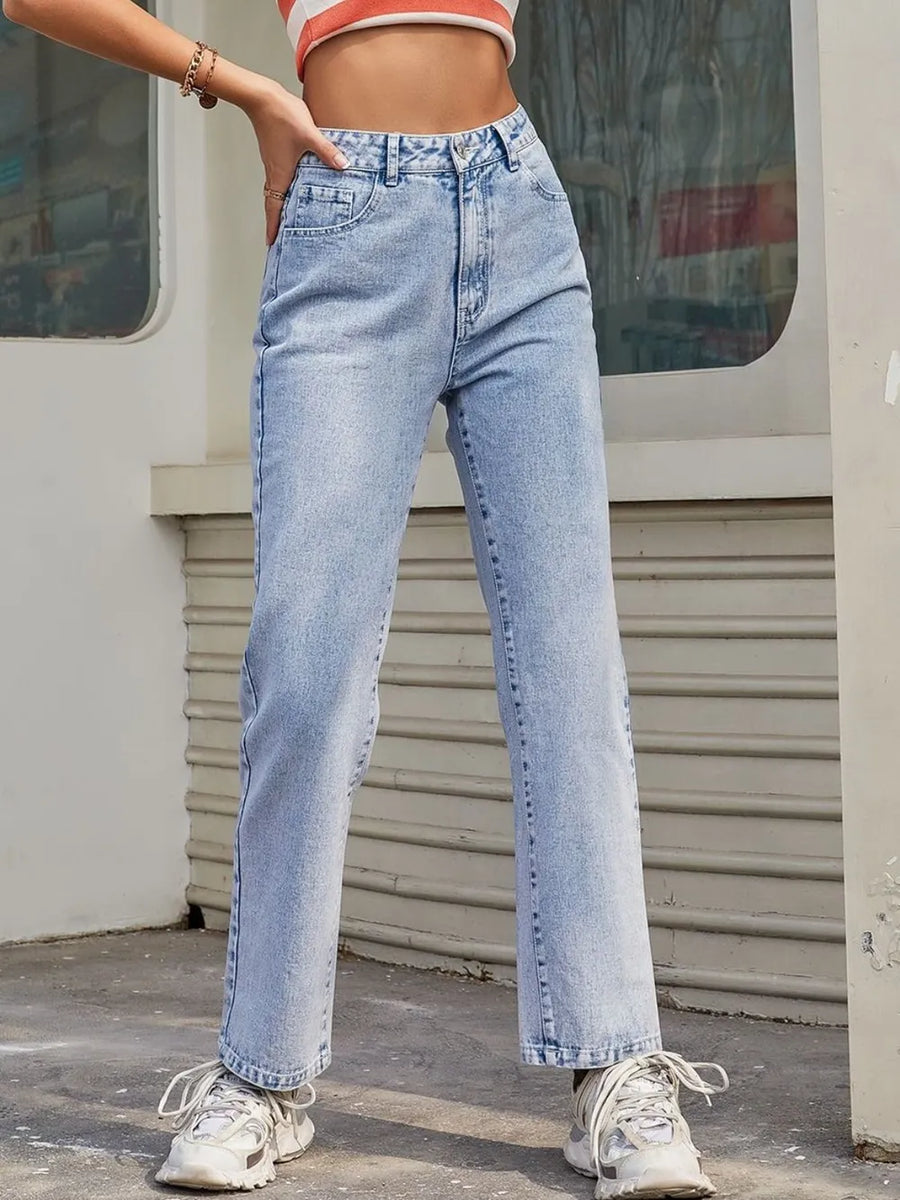 Person wearing light blue jeans and white sneakers in front of a building.