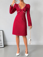 Red dress with a bow detail worn by a person, holding a white handbag against a gray background.