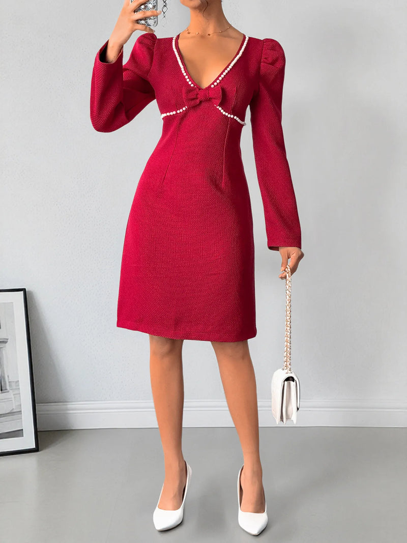 Red dress with a bow detail worn by a person, holding a white handbag against a gray background.