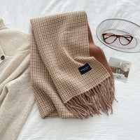 Plaid blanket with tassels on a white surface, next to a glass of water and a pair of glasses.