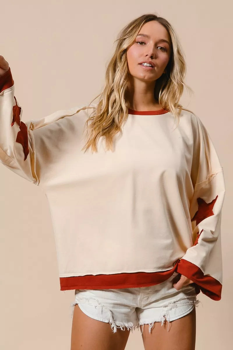 Woman wearing a cream sweater with red accents and denim shorts on a beige background