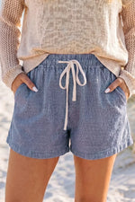 Person wearing blue striped shorts with a beige sweater on a beach.
