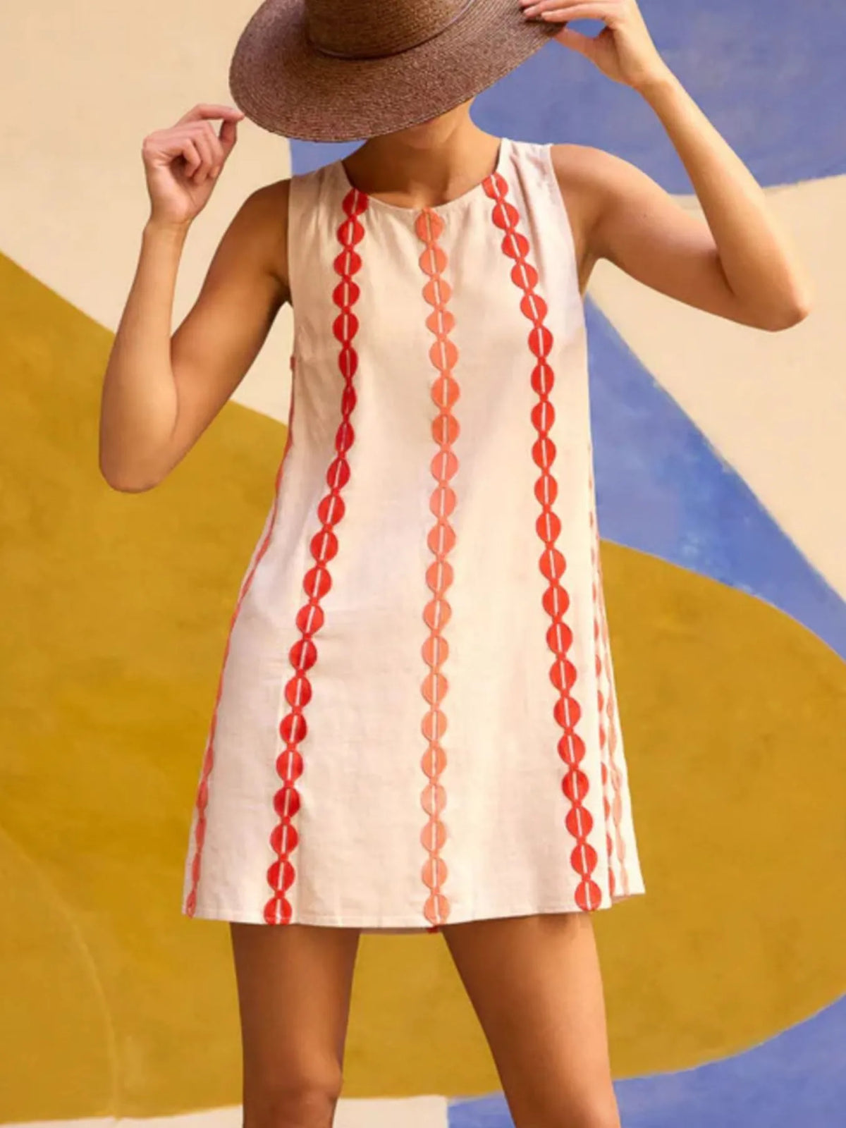 Woman wearing a sleeveless dress with red patterns against a colorful abstract background