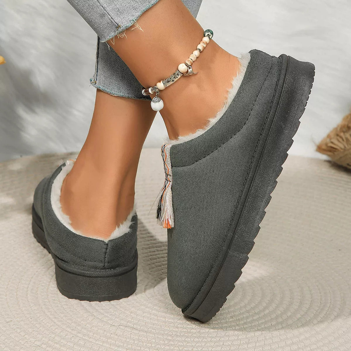 Gray slip-on shoes with fluffy lining worn by a person on a neutral background