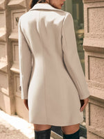 Person wearing a beige coat standing against a textured wall.