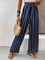 Person wearing navy and white striped pants holding a woven bag against a neutral background