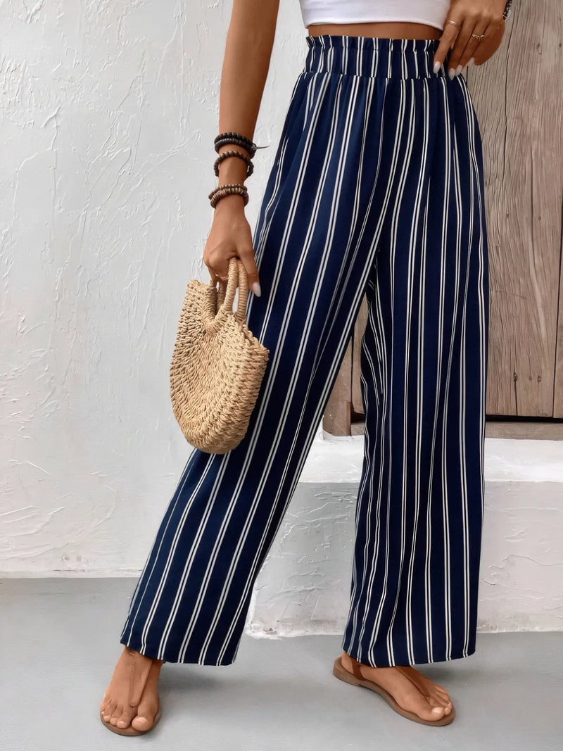 Person wearing navy and white striped pants holding a woven bag against a neutral background