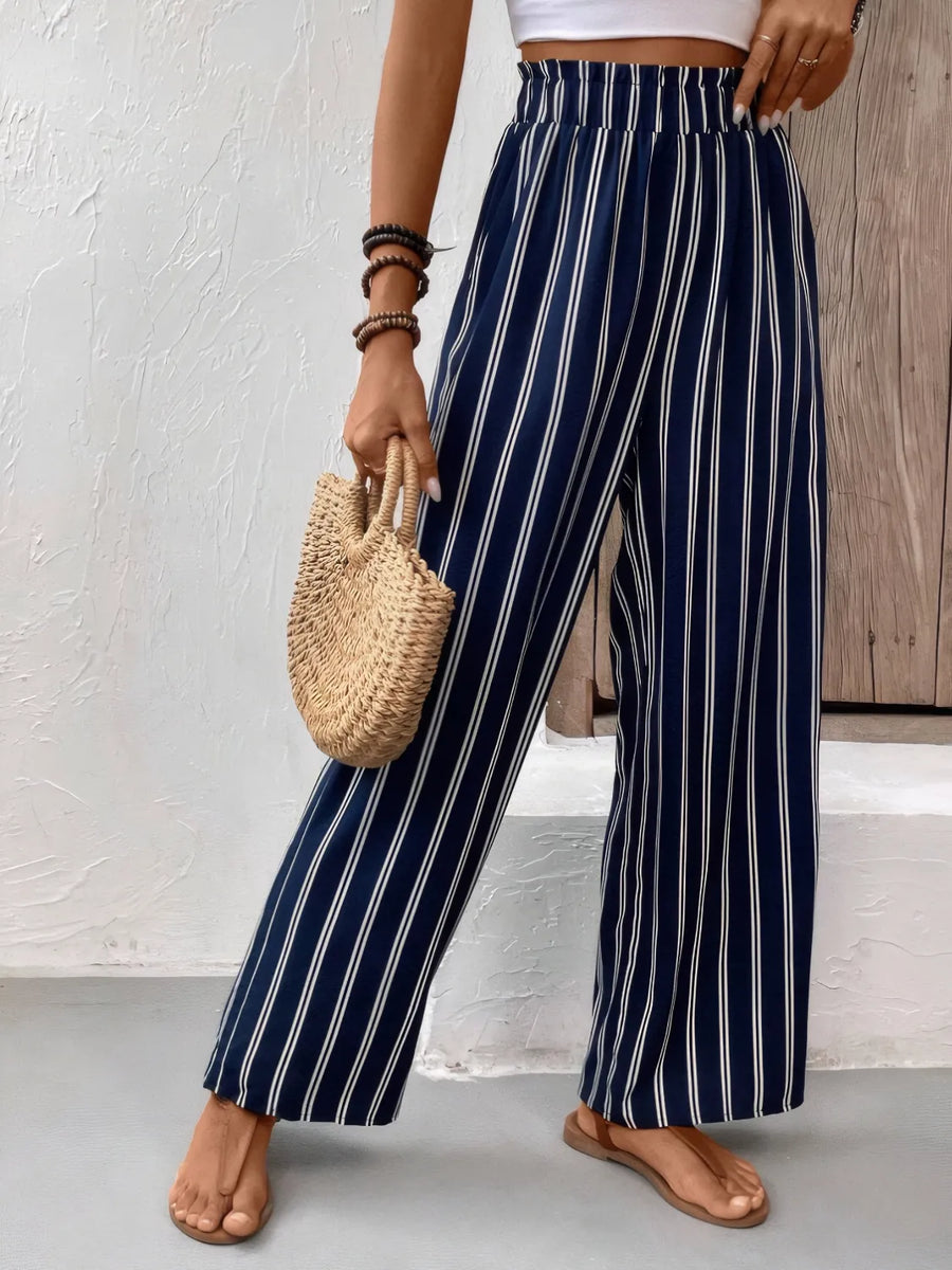 Person wearing navy and white striped pants holding a woven bag against a neutral background