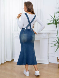 Woman wearing a blue denim dress with white sneakers in a room with white curtains and a plant.