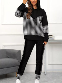 Person wearing a black and white checkered hoodie and pants set in a room with a gray couch.