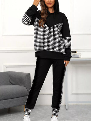 Person wearing a black and white checkered hoodie and pants set in a room with a gray couch.