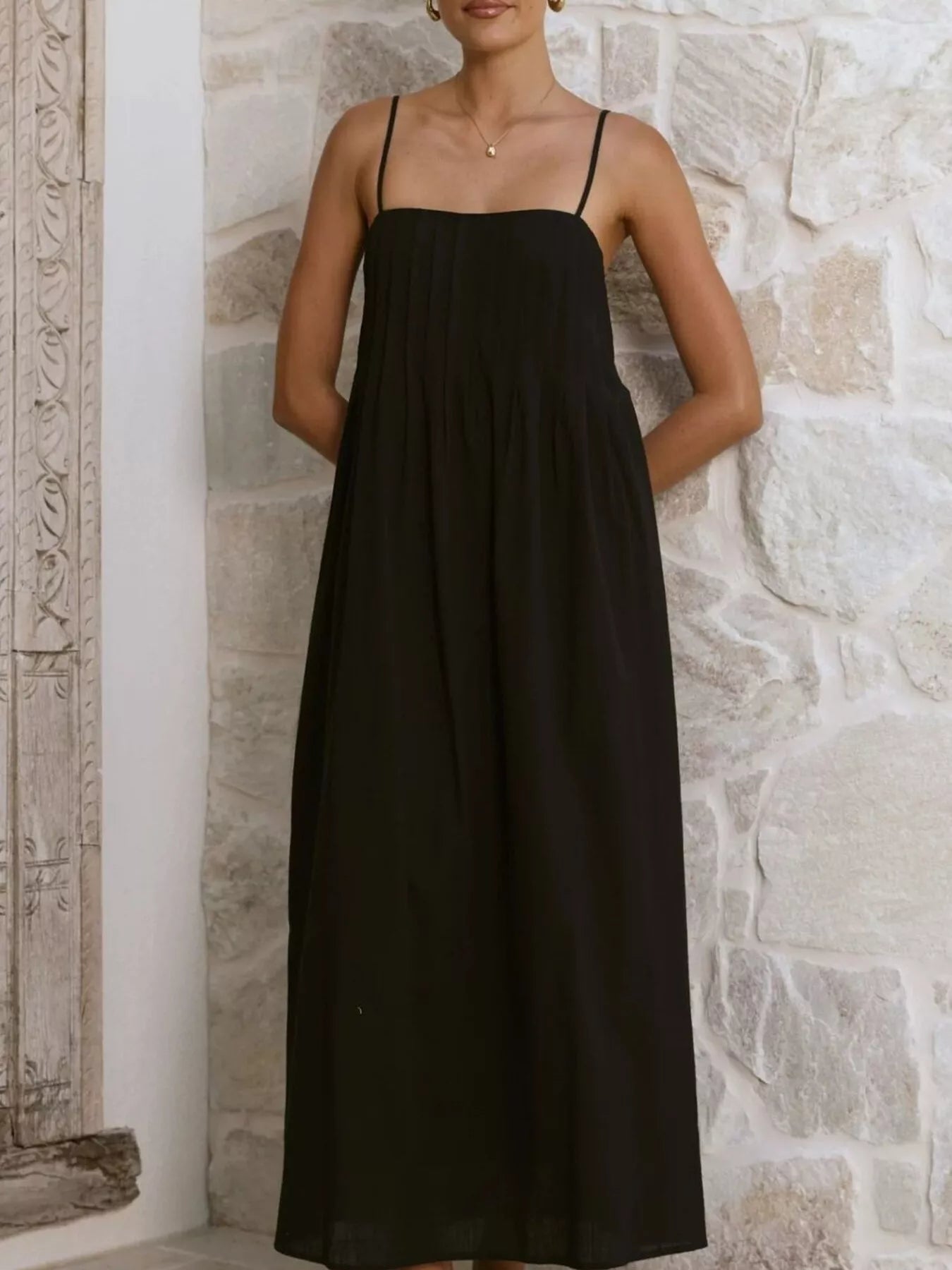 Woman wearing a black dress against a stone wall.