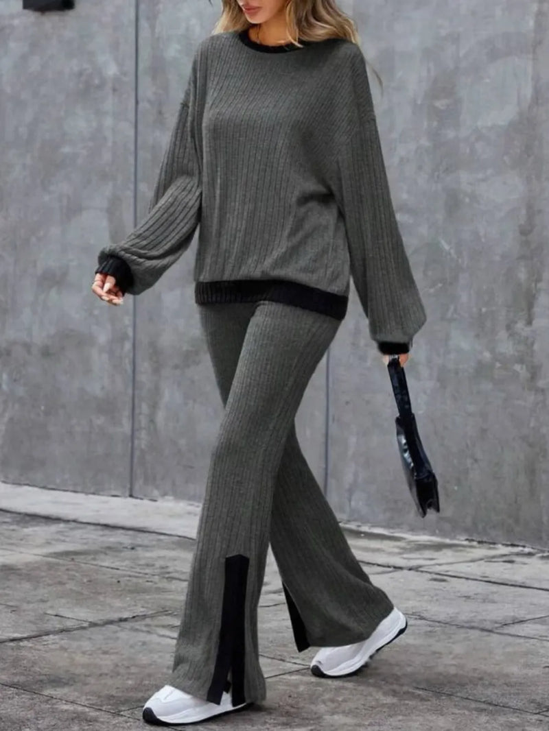 Person wearing a gray sweater and pants with black accents against a gray wall.