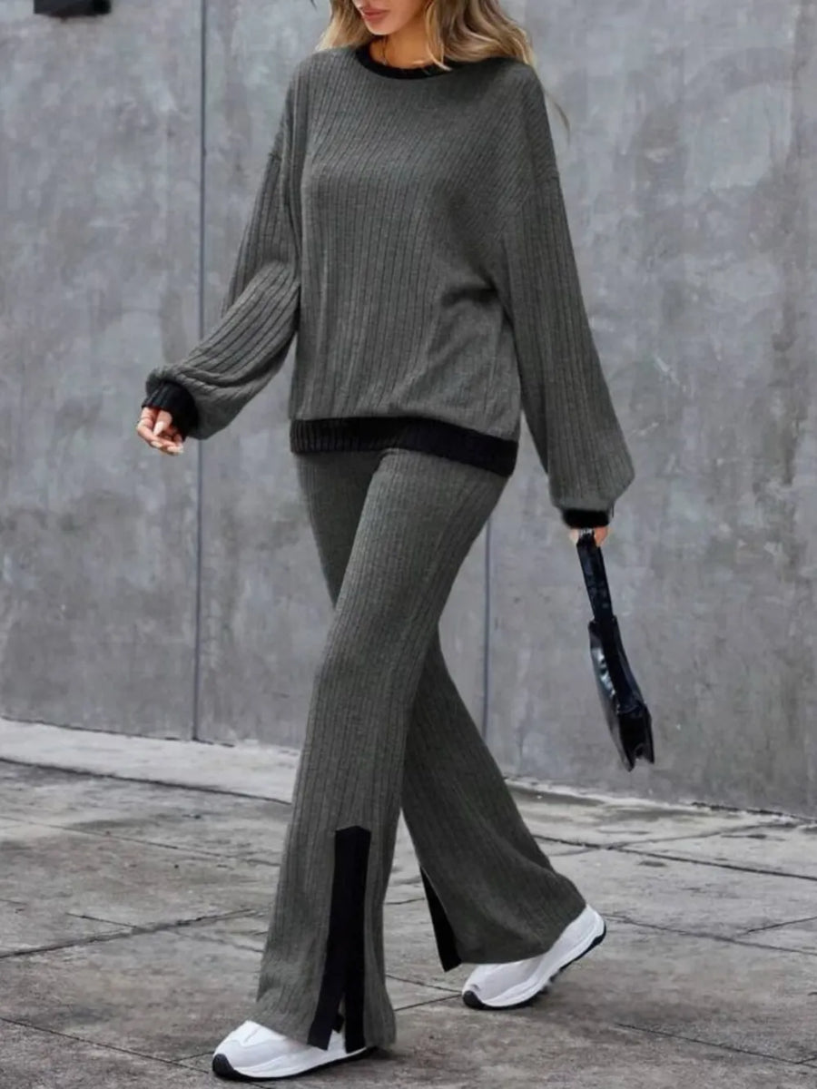 Person wearing a gray sweater and pants with black accents against a gray wall.