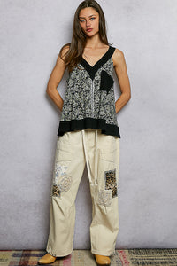 Woman wearing a black and white patterned top with beige pants against a gray background