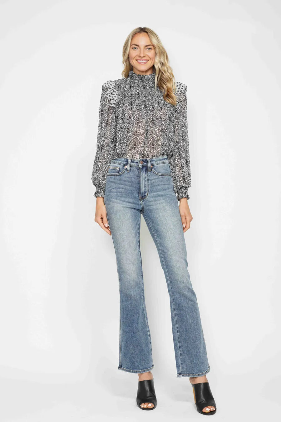 Woman wearing a patterned blouse and jeans on a white background