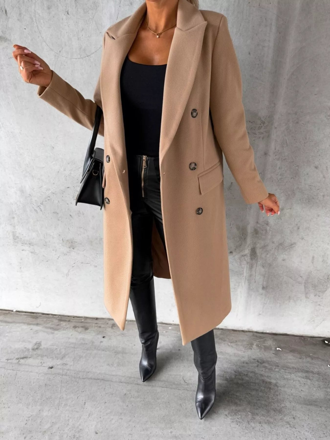 Person wearing a beige coat and black boots against a gray concrete wall.