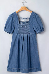 Blue denim dress with puff sleeves on a wooden hanger against a white background