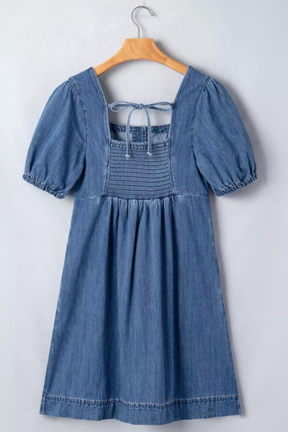Blue denim dress with puff sleeves on a wooden hanger against a white background