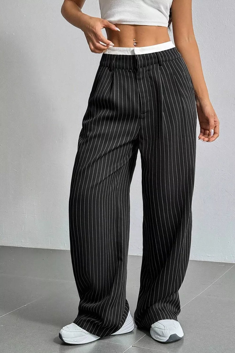 A person wearing black wide-leg pinstripe pants with a white waistband, paired with a white crop top and white sneakers, standing against a light gray wall.