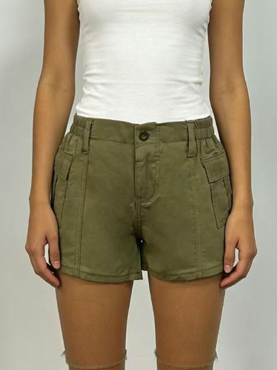 Person wearing olive green shorts and a white top on a plain background
