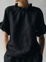 Person wearing a black blouse with ruffled collar against a plain background