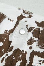 Close-up of a white denim garment with a brown cow-print pattern and a silver snap button closure.