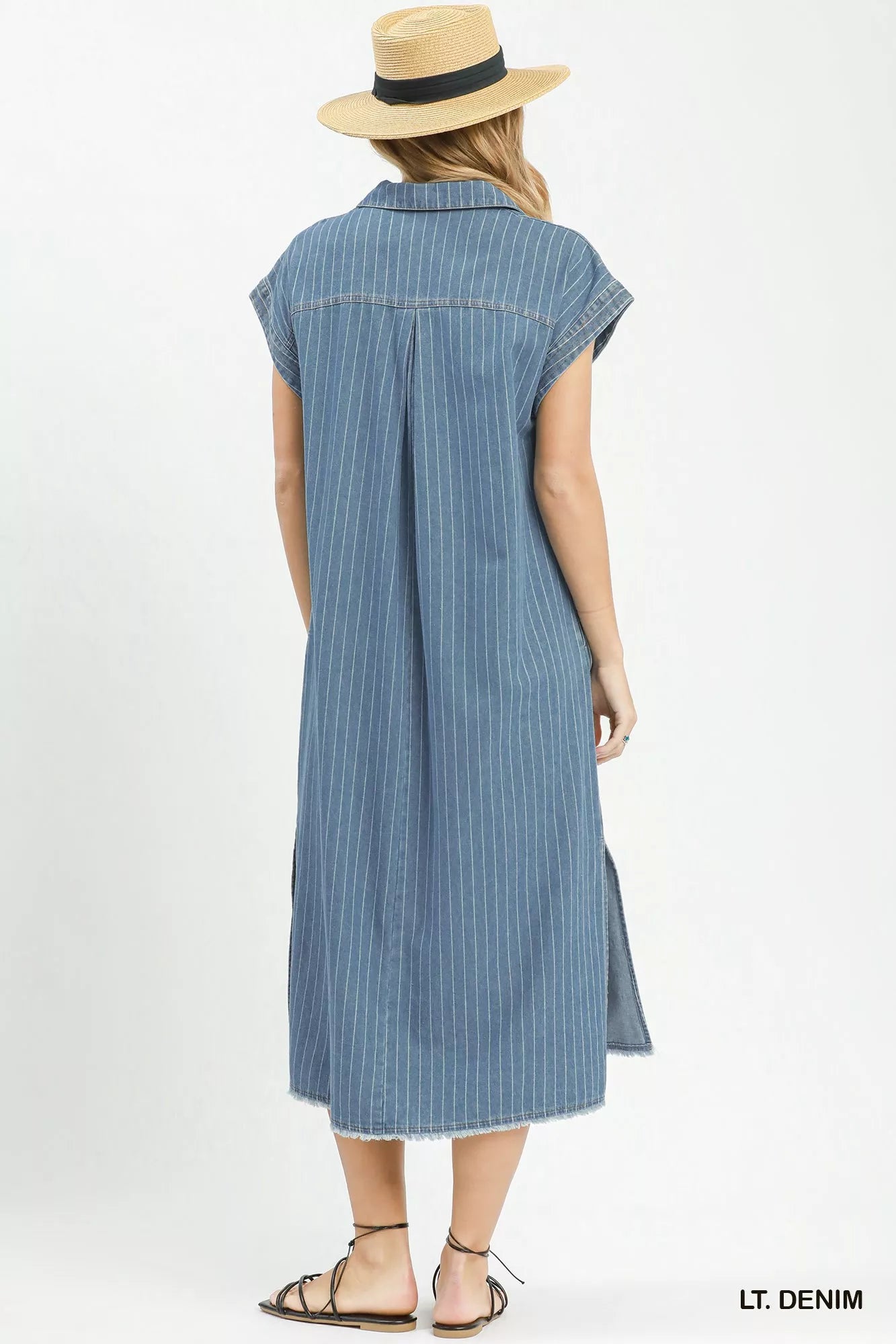 Woman wearing a light denim dress with a straw hat on a white background