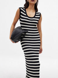 Woman wearing a black and white striped dress holding a textured handbag on a white background