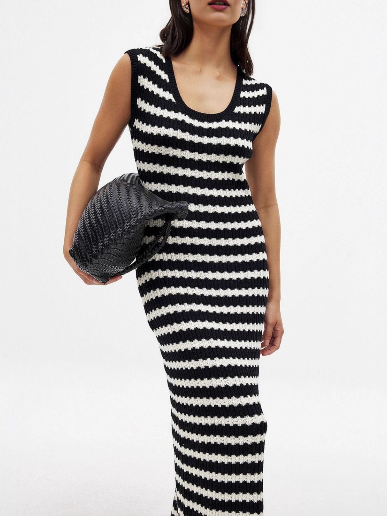 Woman wearing a black and white striped dress holding a textured handbag on a white background