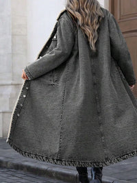 Person wearing a long dark gray coat with a textured texture, standing on a sidewalk.