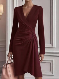 Burgundy dress with long sleeves held by a person against a neutral wall.