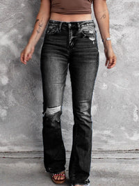 Person wearing black distressed jeans against a gray concrete wall.