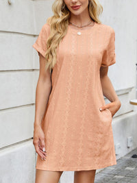 Woman wearing a peach lace dress standing against a light-colored wall.
