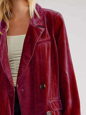Close-up of a person wearing a burgundy velvet jacket on a plain background