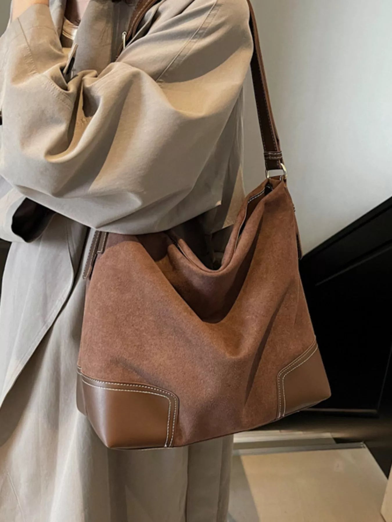 Brown suede handbag held by a person wearing a beige coat.