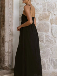 Woman wearing a black dress with cut-out sides against a stone wall.