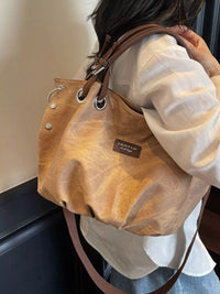 Brown leather handbag with visible brand logo held by a person wearing a white shirt.