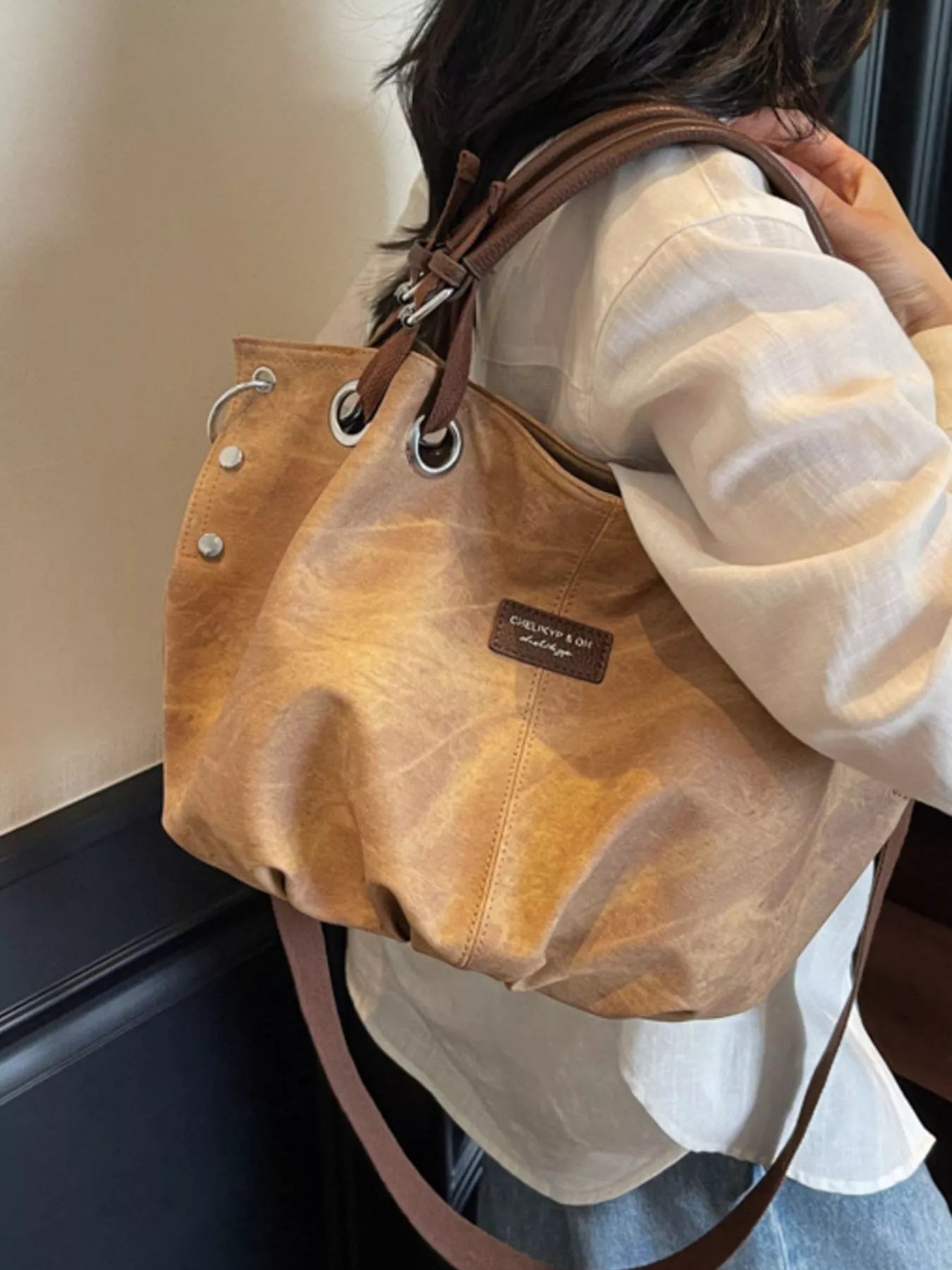 Brown leather handbag with visible brand logo held by a person wearing a white shirt.