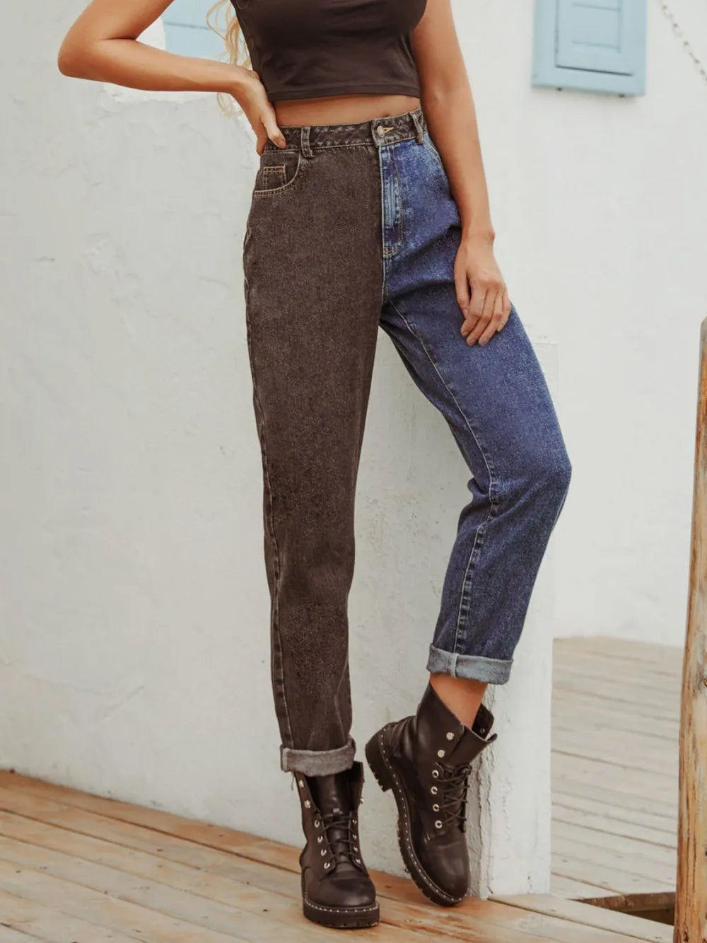 Person wearing a brown top, dark gray jeans, and black boots against a white wall.