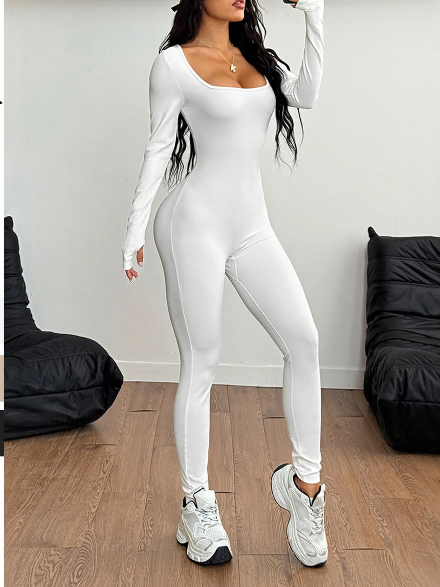 Person wearing a white jumpsuit standing in a minimalistic room with black chairs.