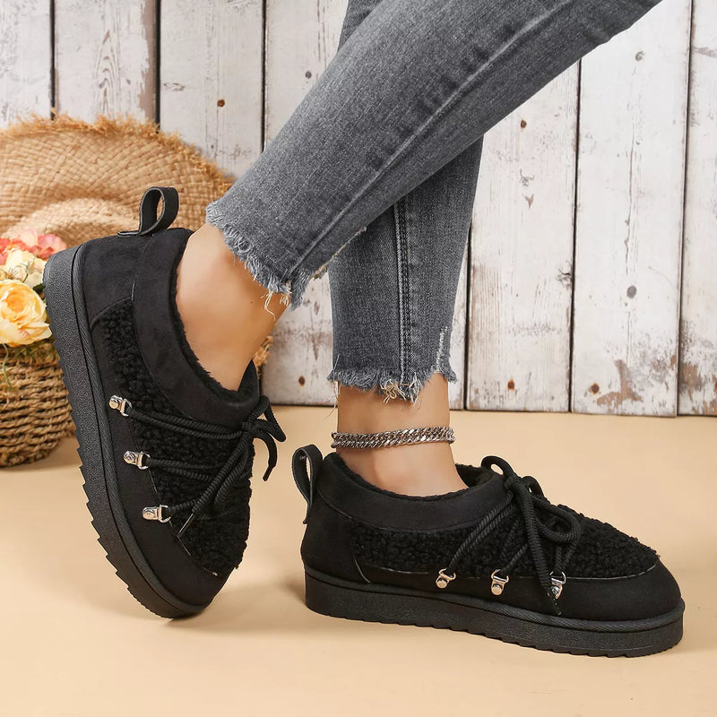 Black sneakers worn with gray jeans on a wooden floor.