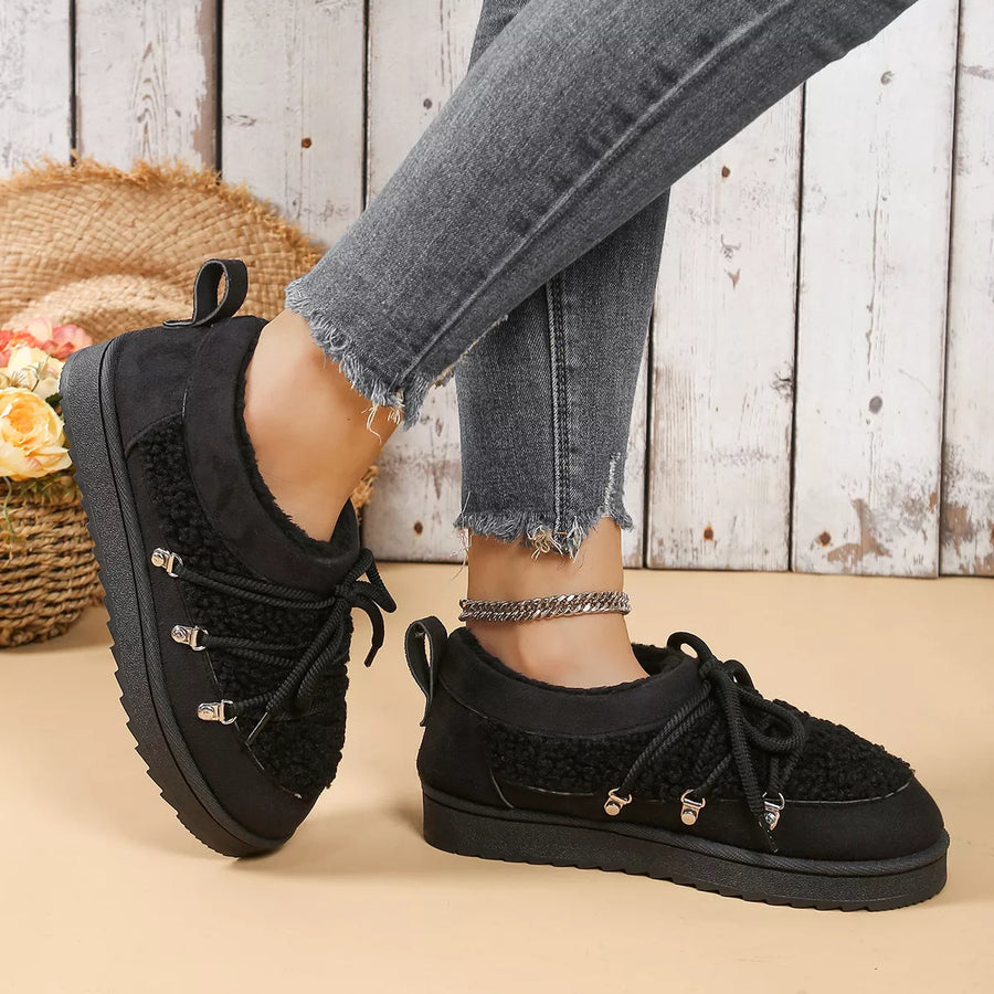 Black sneakers worn with gray jeans on a wooden floor.