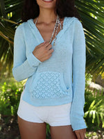 Woman wearing a light blue knitted hoodie with a textured pocket against a natural background.
