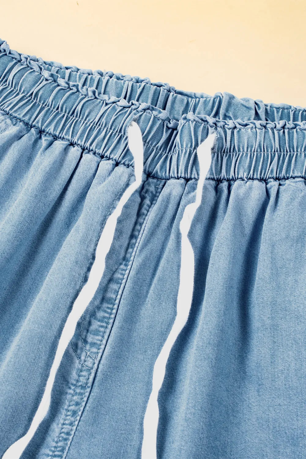 Close-up of light blue denim shorts with white drawstring on a beige background